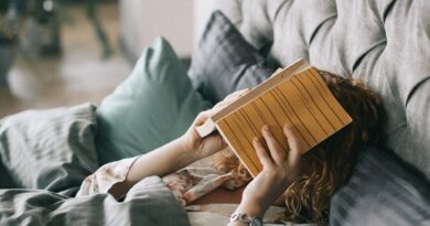 Woman Covering Face With Book on Bed