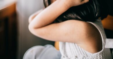 Side view of stressed unrecognizable little girl with black hair sitting at round table and touching head