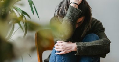 Anonymous young sorrowed female in casual outfit touching dark hair and embracing knees while sitting on chair at home. Violencia machista