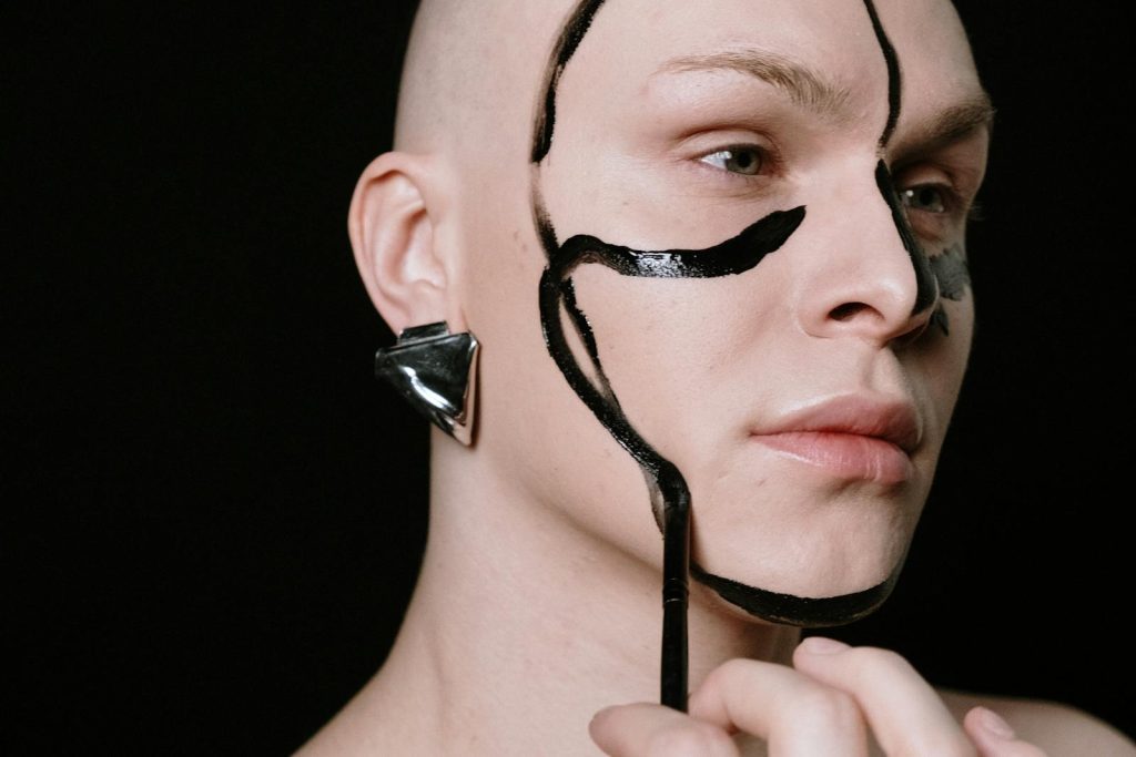 Creative portrait of a person with bold face paint and metallic earring on a black background. Género.