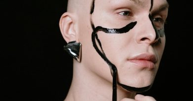 Creative portrait of a person with bold face paint and metallic earring on a black background. Género.