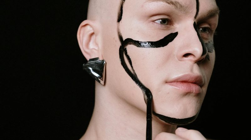 Creative portrait of a person with bold face paint and metallic earring on a black background. Género.