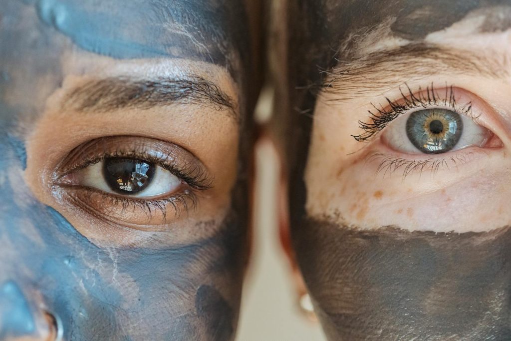 Closeup portrait of two women with facial masks, highlighting diversity and skincare routines. Gender